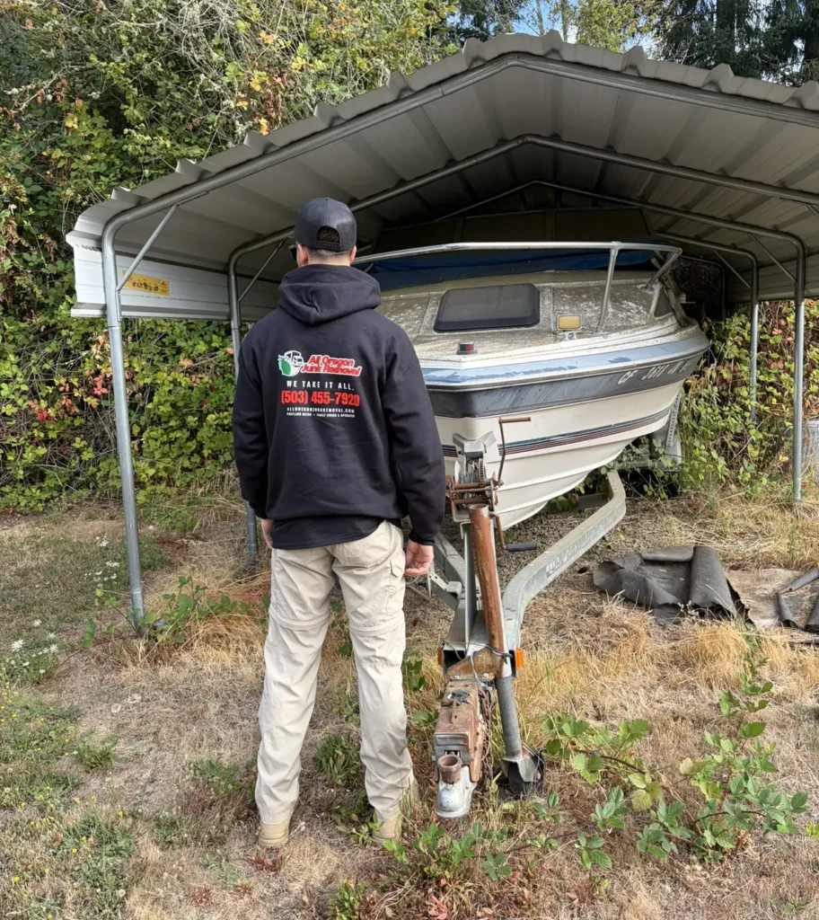 All Oregon Junk Removal crew member in a branded hoodie assessing a boat for removal from a carport