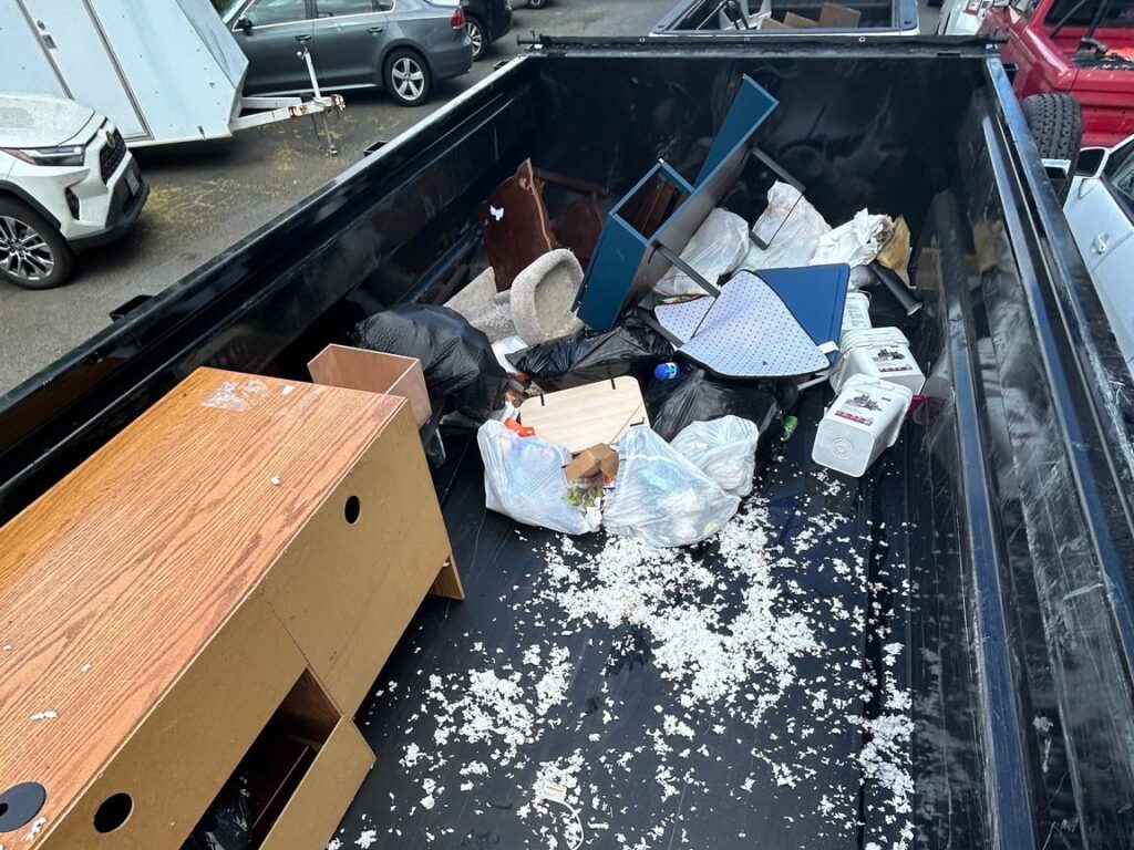 Bagged trash, a desk and loose debris loaded in an All Oregon Junk Removal dump trailer