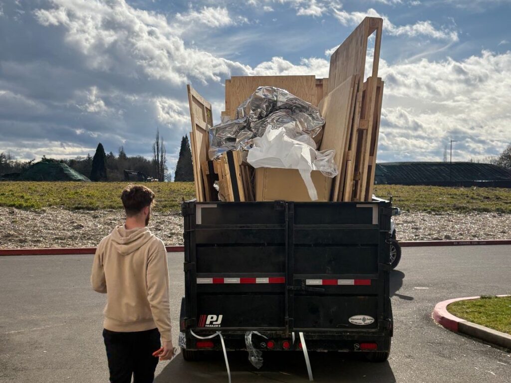 All Oregon Junk Removal crew member walking to a dump trailer loaded with construction debris and lumber